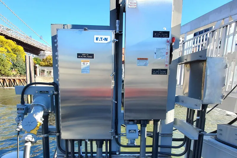 Stainless steel electrical enclosures and shore power connections installed on a NYC Ferry landing barge, Brooklyn Bridge in the background.