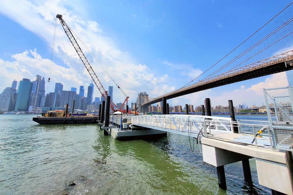 Crane barge and completed gangway at the DUMBO/Fulton Ferry landing under construction, Brooklyn Bridge behind.