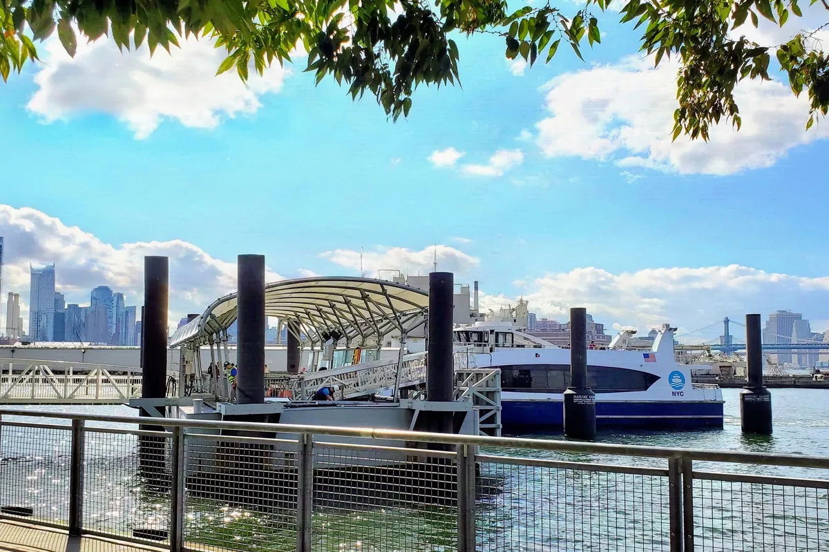 Canopy-topped ferry landing at South Williamsburg with an NYC Ferry moored alongside and the Manhattan skyline beyond.