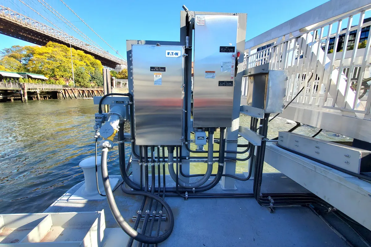 Stainless steel electrical enclosures and shore power connections installed on a NYC Ferry landing barge, Brooklyn Bridge in the background.