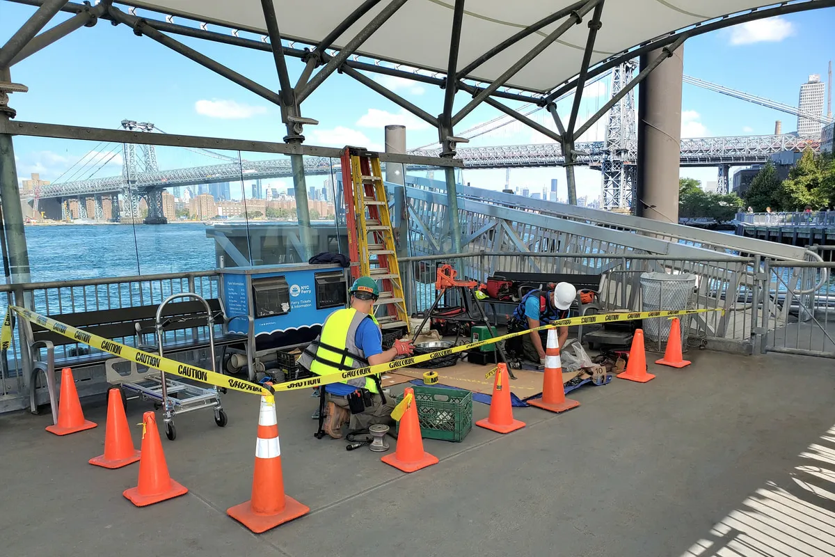 Electricians working on electrical systems at the South Williamsburg ferry landing, Williamsburg Bridge in the background.